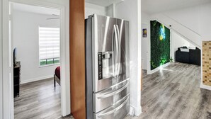 Eine moderne Küche mit Edelstahl-Kühlschrank, Holzelementen und einer grünen Wand mit Pflanzen.