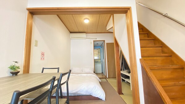 A compact room with a wooden dining table, a bed, and a staircase.