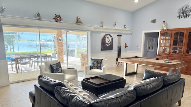 Un salon avec une table de billard, un canapé en cuir et une vue sur une piscine à l’extérieur.