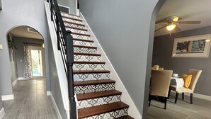 Eine Treppe mit gemusterten Stufen und einem modernen Geländer, die zu einem Essbereich mit Stühlen und einem Tisch führt.