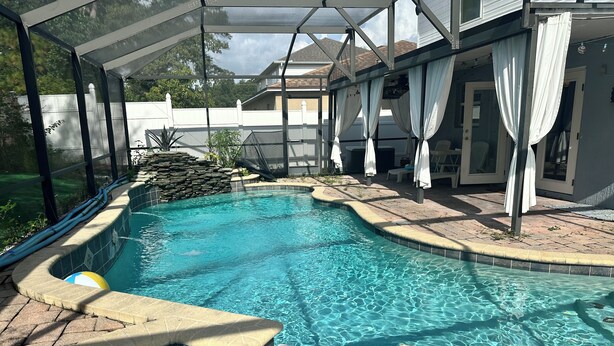 Ein Schwimmbecken mit Steinbord, eine Lounge-Bereich mit Sonnenschirmen und ein überdachter Bereich mit Blick auf den Garten.