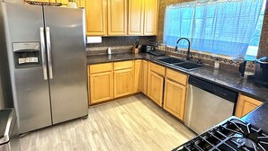 Una cocina moderna con armarios de madera, un refrigerador de acero inoxidable, una estufa a gas y un ventanal con cortina azul.
