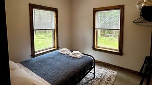 Een slaapkamer met een bed, twee ramen, een plafondventilator en een vloerkleed.