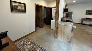 Een ruime woonkamer met een keuken, een houten deur, een witte wasmachine en een vloerkleed.