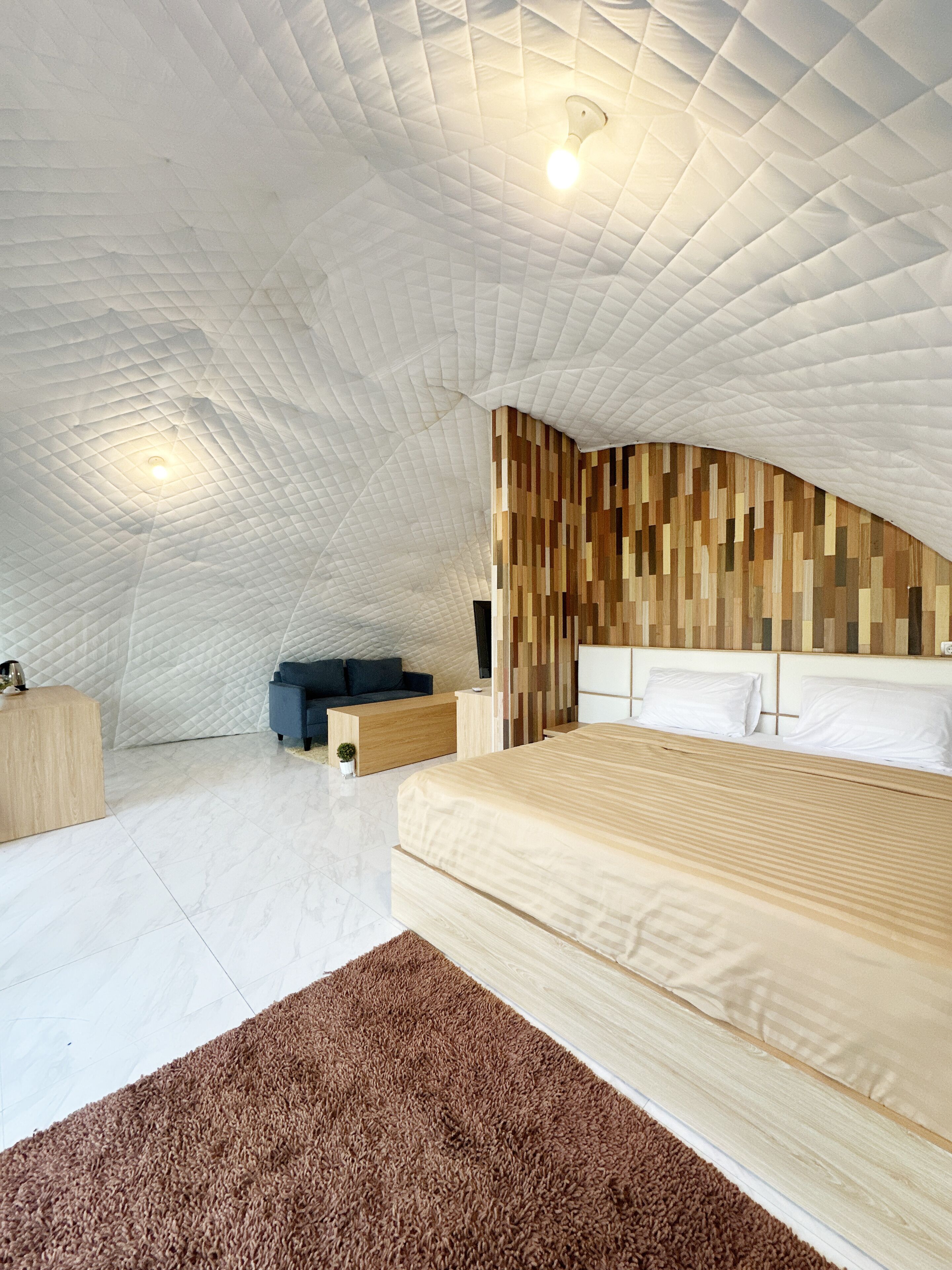 A bedroom with a unique arched ceiling, a wooden headboard, a bed with white linens, a small seating area, and a wooden dresser.