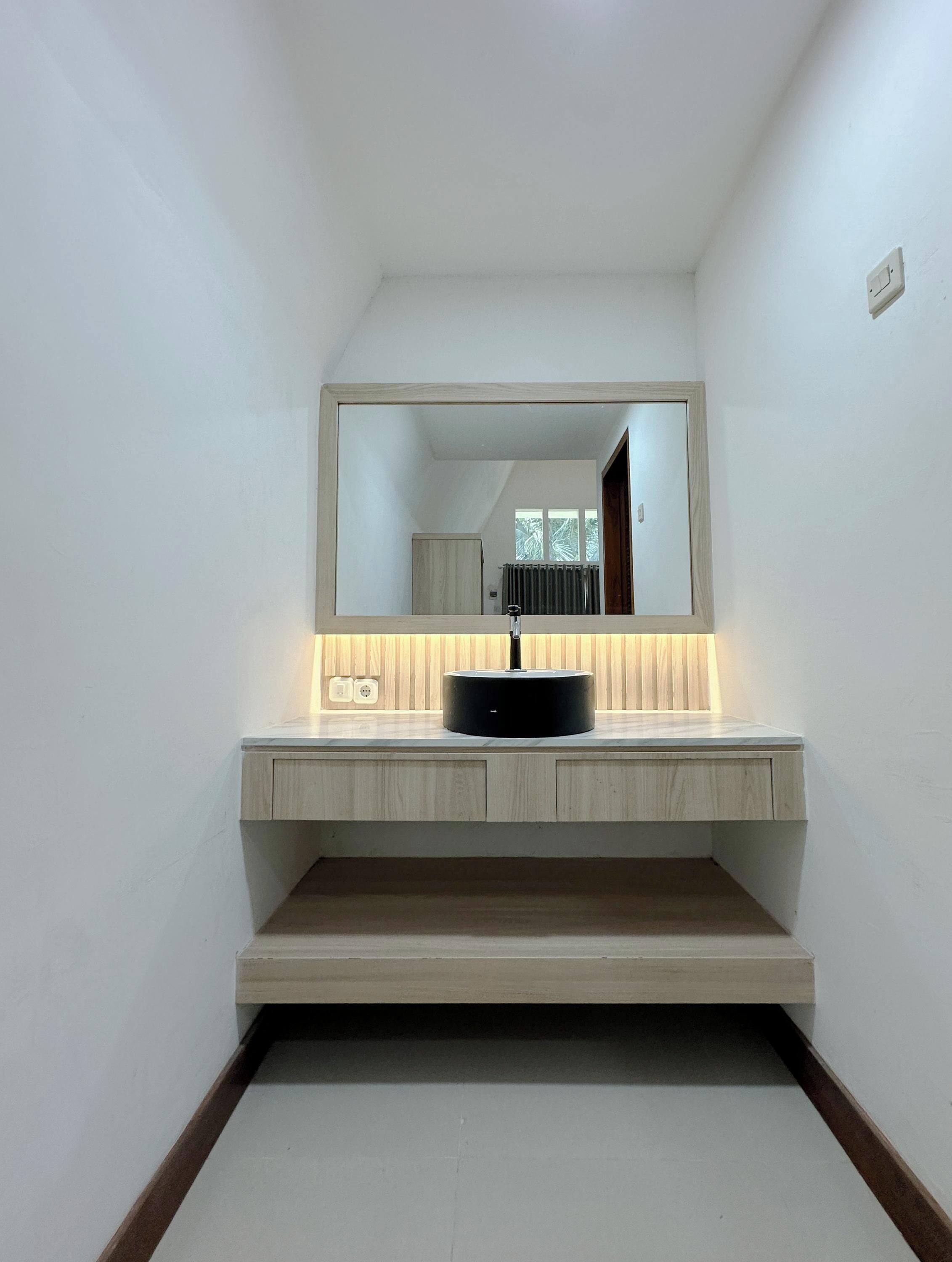 Une salle de bain moderne avec un grand miroir, un lavabo noir et des meubles en bois.
