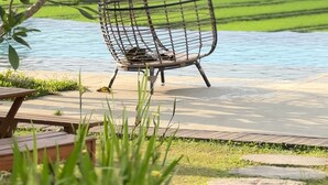 Silla hamaca junto a una masa de agua con un paisaje verde al fondo.