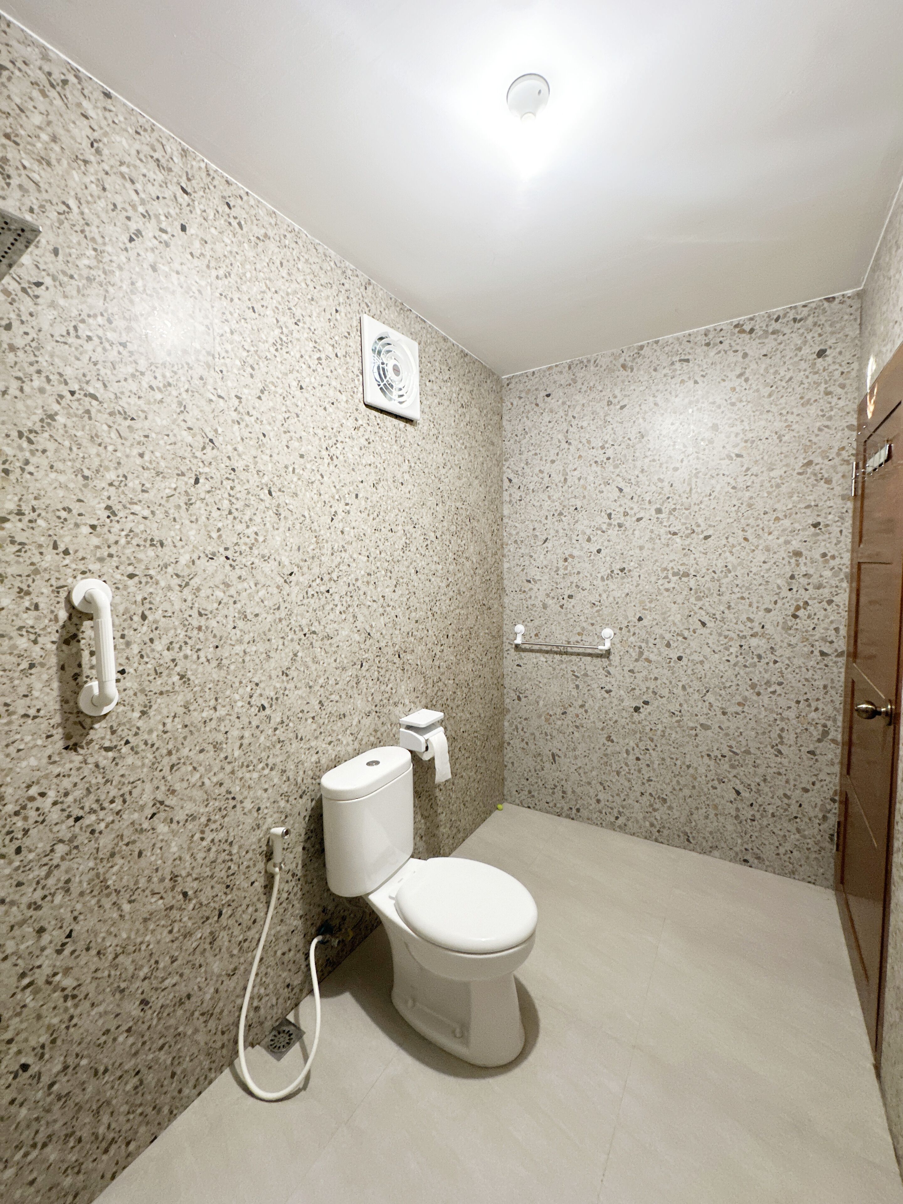 Une salle de bain avec des toilettes blanches, un ventilateur fixé au mur et un porte-serviettes.