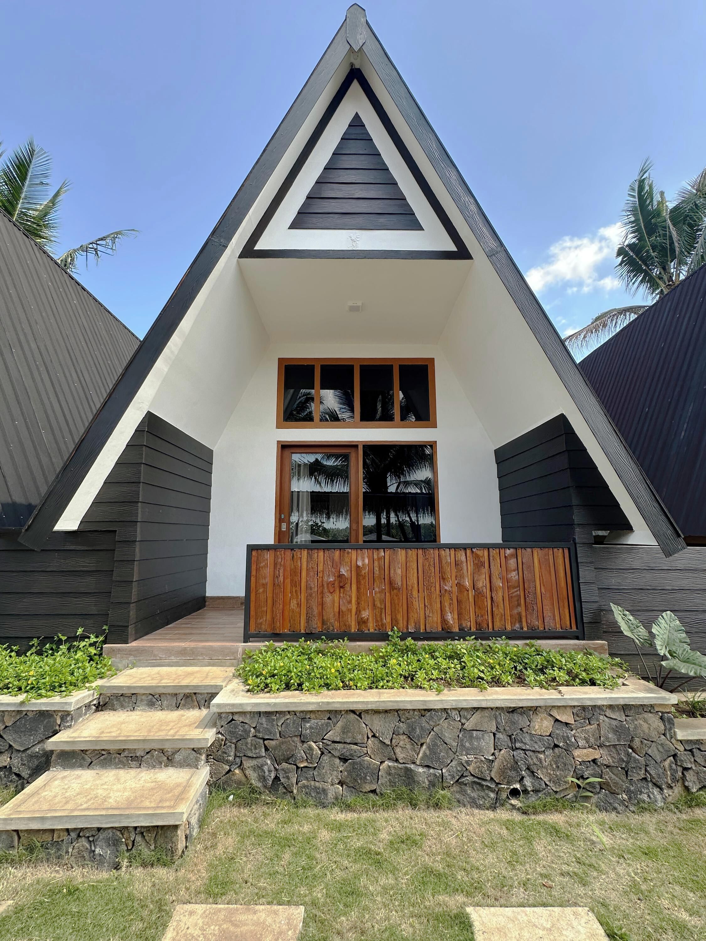 Un edificio moderno con techo triangular, amplios ventanales y una terraza de madera.