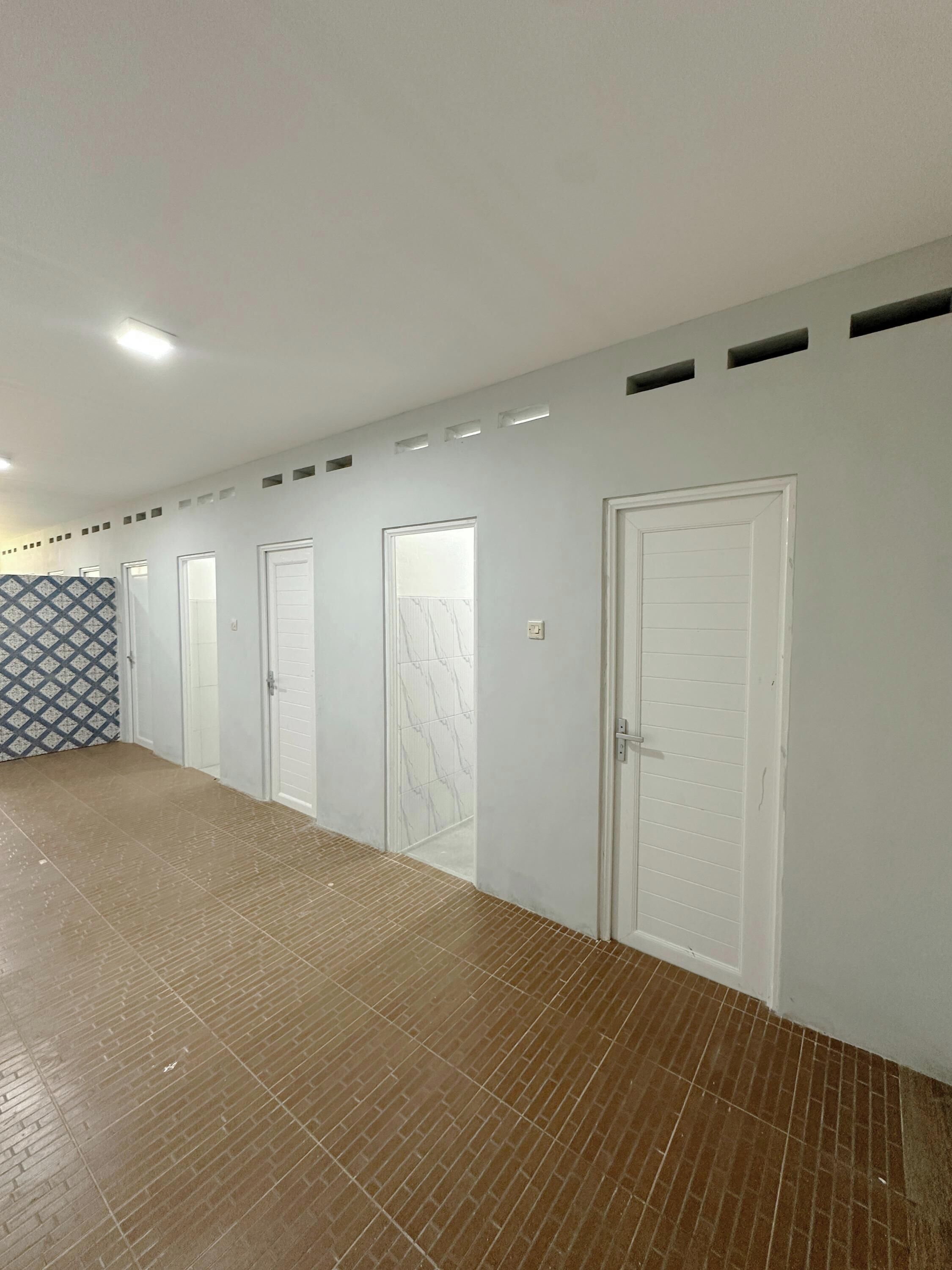 Ein Flur mit mehreren weißen Türen, einer Wand mit Muster und einem gefliesten Boden.