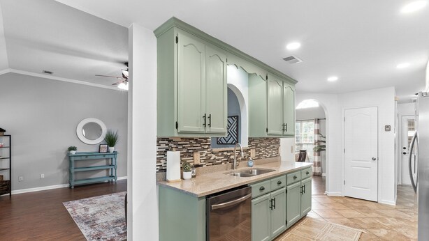 A kitchen with green cabinets, a dishwasher, and a tiled backsplash.