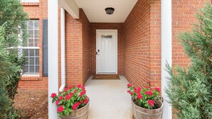A brick building with a white door, two wooden planters with red flowers, and a white porch with a ceiling light.