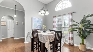 A dining area with a table set for four, wooden chairs, a chandelier, and a potted plant.
