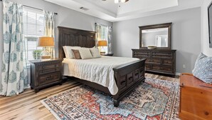 A bedroom with a large bed, wooden headboard, nightstands, a dresser, a mirror, and a ceiling fan.