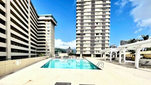 A rooftop swimming pool with lounge chairs and a view of tall buildings.