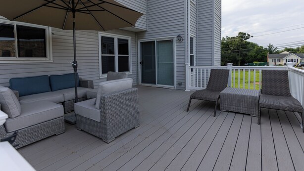 A covered deck with wicker furniture, including a sofa and chairs, and a large umbrella. - Bring the whole family to Unique Luxury Home, it is simply home away from home. (Randallstown)