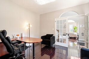 A modern room with a wooden table, two black chairs, a standing lamp, and a glass door leading to another room.
