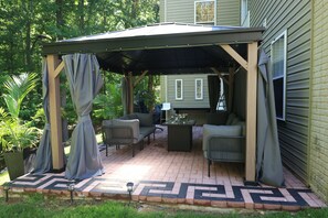 A covered patio area with seating, a table, and a potted plant.
