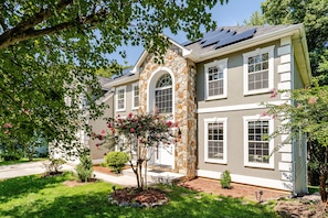 A two-story house with a stone facade, multiple windows, and solar panels on the roof. - The Royal Estate (Fort Washington)
