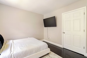 A bedroom with a bed, a television mounted on the wall, and a door. - The Royal Estate (Fort Washington)