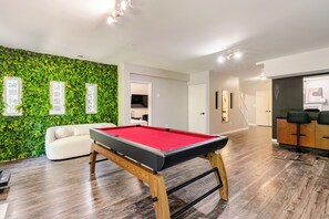 A pool table in a room with a green wall and a white sofa.