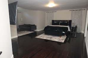A modern bedroom with a large bed, a sofa, a small table, and a mirror.