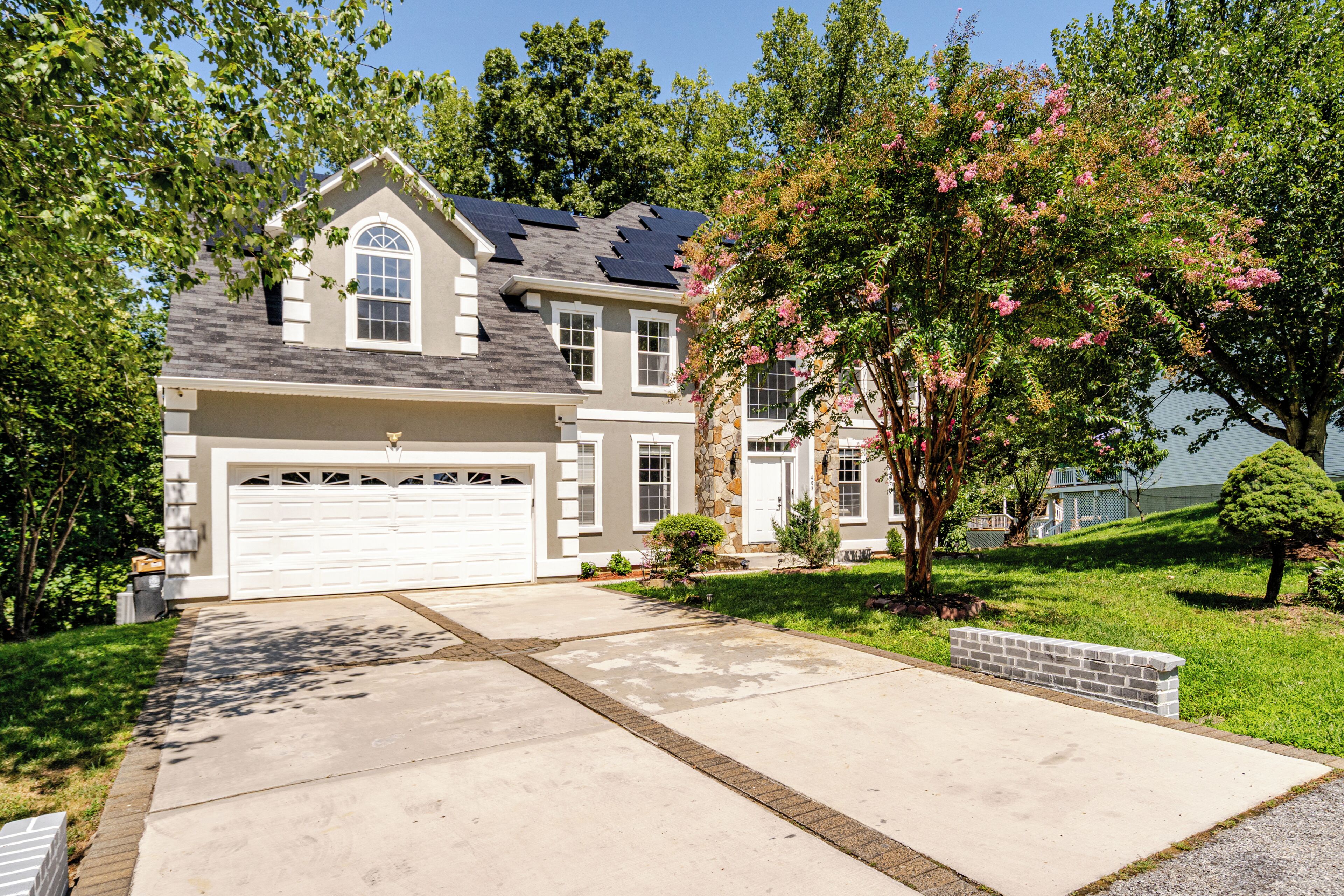 A two-story house with a garage, a stone facade, and a well-maintained lawn.