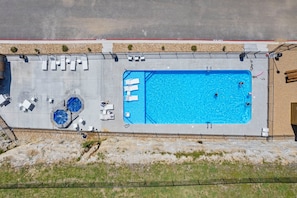 An aerial view of a swimming pool with lounge chairs and a small hot tub area.