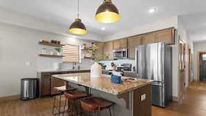 A modern kitchen with a central island, stainless steel appliances, wooden cabinets, and pendant lighting.