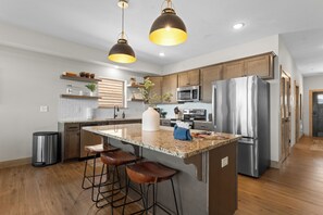 A modern kitchen with a central island, stainless steel appliances, wooden cabinets, and pendant lighting.