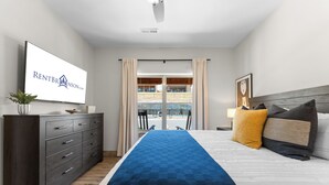 A hotel room with a bed, a dresser, a television displaying a website, and a view of an outdoor area.