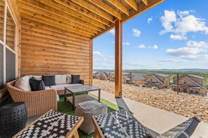 A wooden cabin with a covered porch, furnished with wicker furniture and a view of a residential area.