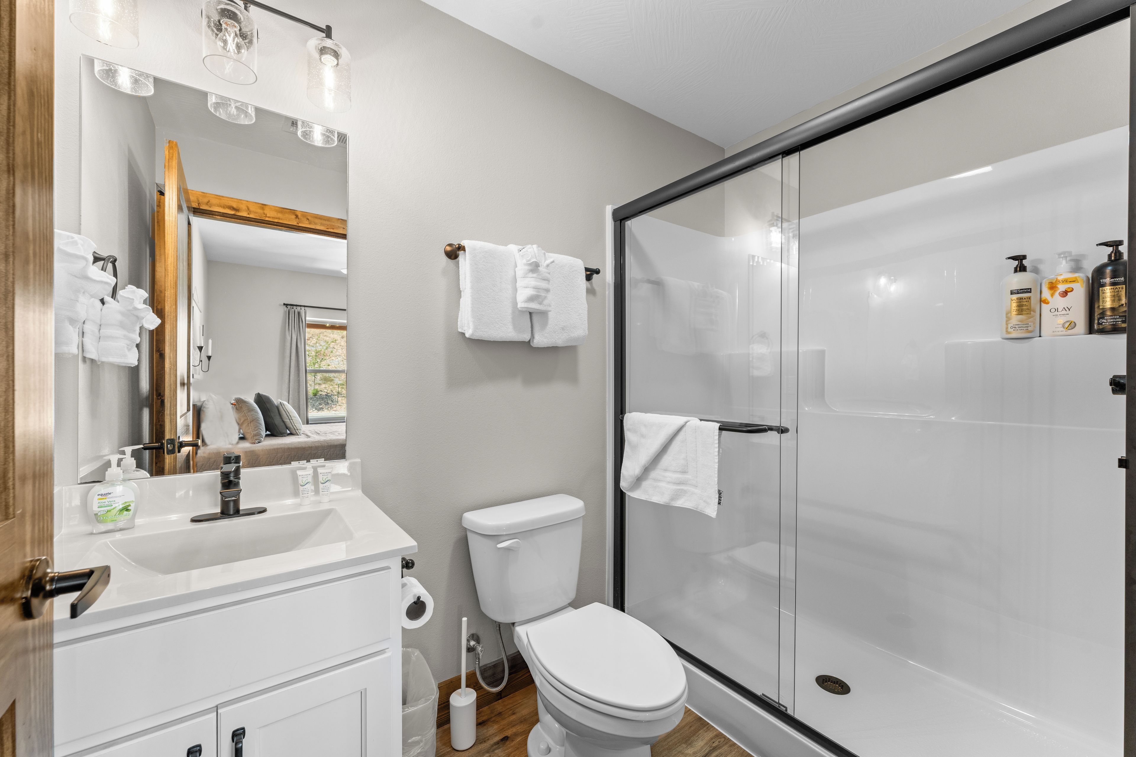 A bathroom with a glass-enclosed shower, a white toilet, a sink with toiletries, and a mirror with a wooden frame.