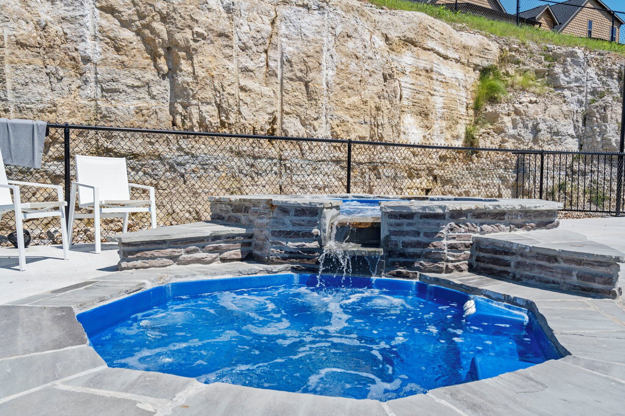 A swimming pool with a waterfall feature, surrounded by stone steps and a black metal fence.