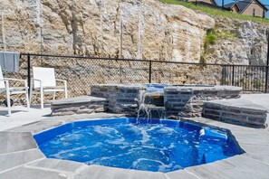 Una piscina con una cascada, rodeada de escalones de piedra y una cerca de metal negro.