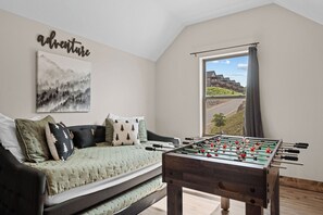 A cozy room with a sofa, a foosball table, a painting, and a window with a view of buildings.
