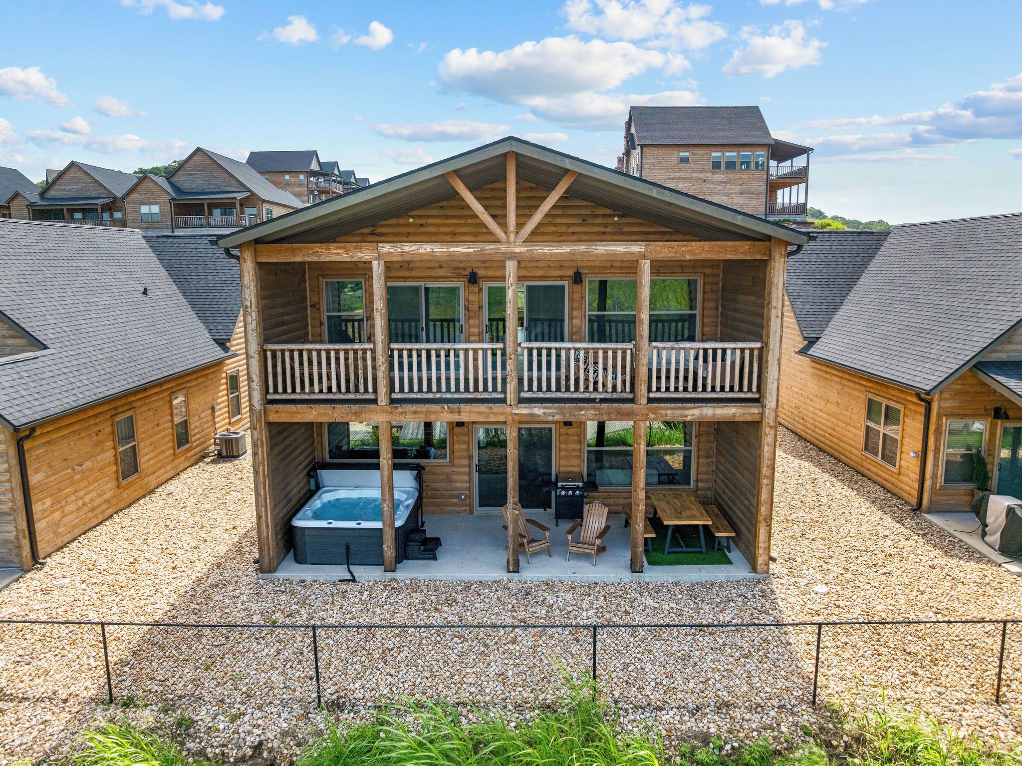 A two-story wooden cabin with a balcony, a hot tub, and outdoor seating.