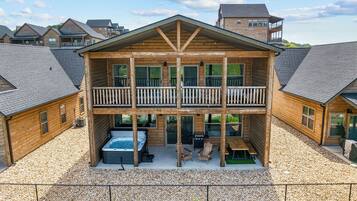 A two-story wooden cabin with a balcony, a hot tub, and outdoor seating.