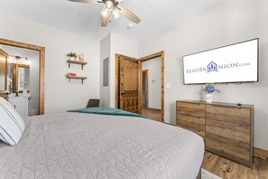 A bedroom with a bed, a television, a dresser, and a ceiling fan.
