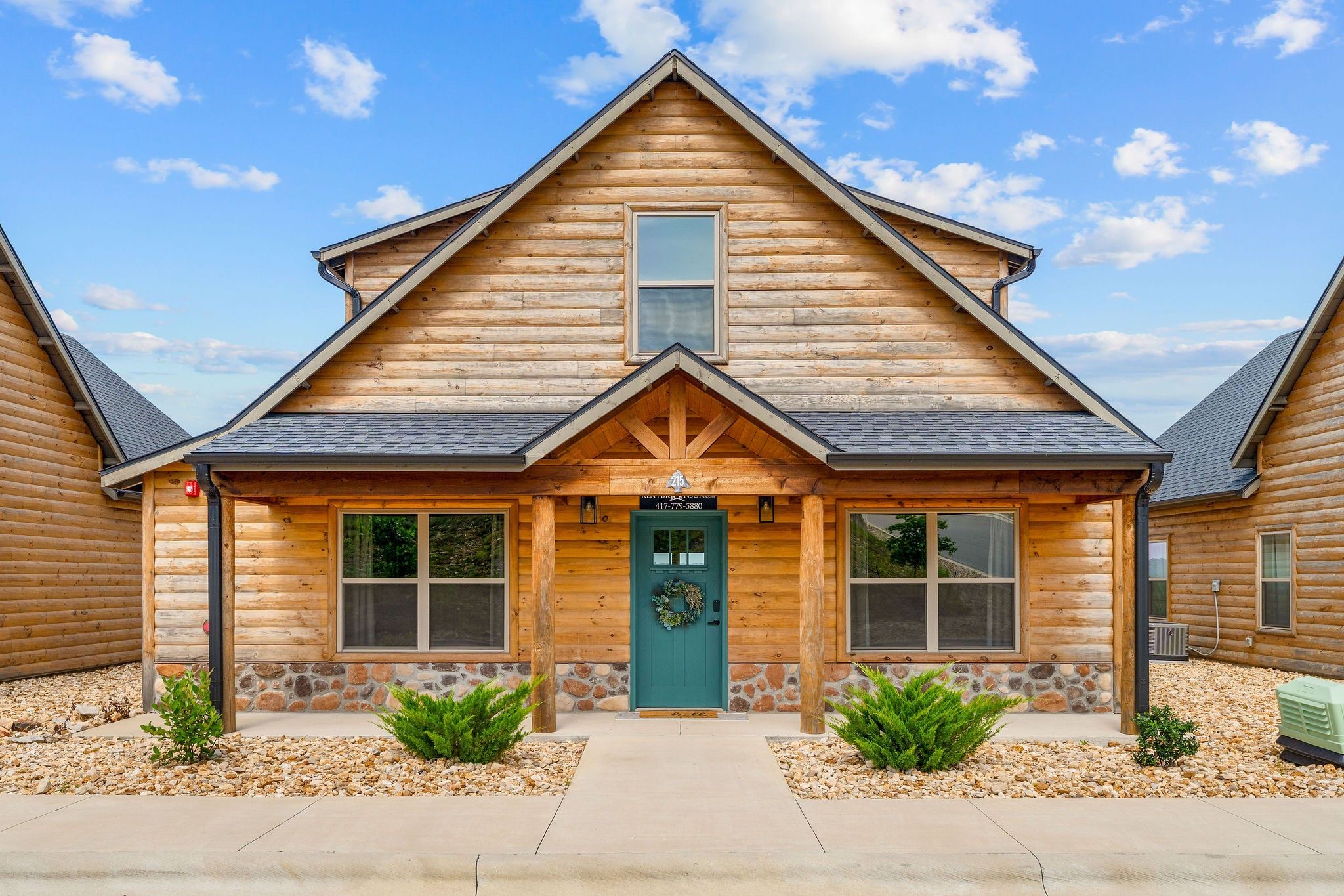 A log cabin with a green door, stone foundation, and a small porch with plants.