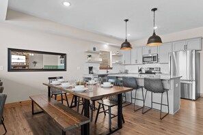Una cocina moderna con comedor, que incluye electrodomésticos de acero inoxidable, una mesa de comedor de madera e iluminación colgante.
