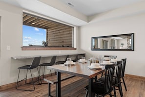 A dining area with a long table, black chairs, and a window with a view.