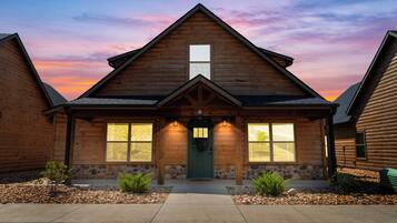 A log cabin with a stone foundation, a green door, and a small porch with potted plants.