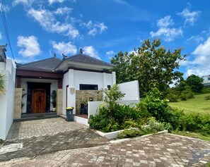 A modern house with a stone facade, a wooden door, and a paved driveway leading to the entrance.