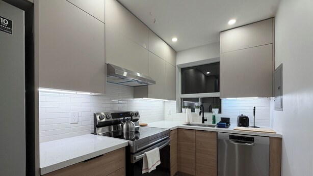 A modern kitchen with stainless steel appliances, wooden cabinets, and a white tiled backsplash. - Leaside 2BR with parking and laundry, family and pet friendly neighbourhood (Toronto)