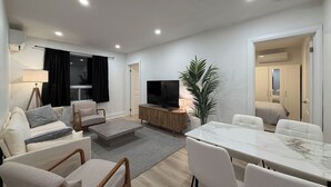 A modern living room with a sofa, armchairs, a coffee table, a TV, and a dining table with chairs. - Leaside 2BR with parking and laundry, family and pet friendly neighbourhood (Toronto)