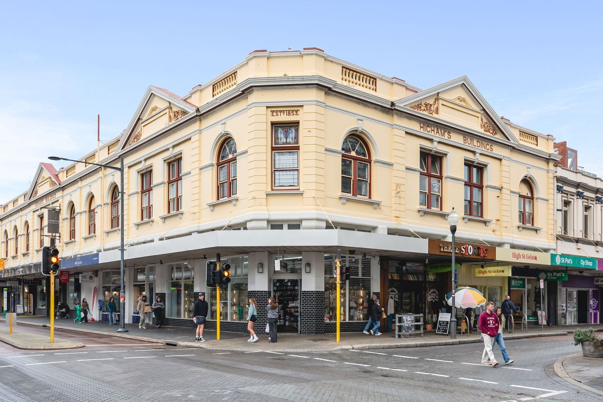 A historic building with a corner entrance, multiple storefronts including 'Three Stores' and 'High St Gelato', and a pedestrian crossing.