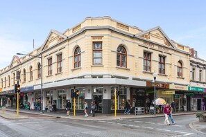 A historic building with a corner entrance, multiple storefronts including 'Three Stores' and 'High St Gelato', and a pedestrian crossing.