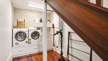 A laundry room with two front-loading washing machines, a drying rack, and a wooden staircase.
