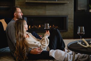 A couple sitting on a couch in front of a fireplace, holding wine glasses.